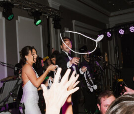 Bride and groom toss beaded necklaces to cheering guests at a lively Louisiana wedding with a live band.