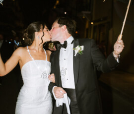 Bride and groom kiss at night with lace umbrellas at their Gulf South wedding, wearing medallions and classic attire.