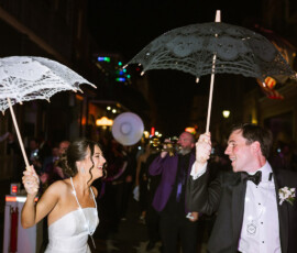 Bride and groom dance joyfully in the street at night with umbrellas, band, and lights at a lively New Orleans wedding.