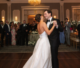 Bride and groom dance at a Louisiana wedding, watched by smiling guests under a chandelier in an elegant New Orleans venue.
