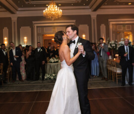 Bride and groom share their first dance in a classic New Orleans ballroom, surrounded by elegant guests, chandeliers, and flowers.
