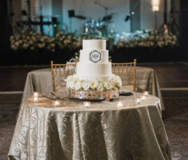 Three-tiered white wedding cake with flowers on a decorated table, candles, and a festive New Orleans-inspired backdrop.