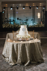 Three-tiered white wedding cake with flowers on a decorated table, candles, and a festive New Orleans-inspired backdrop.