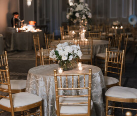 Elegant event room with round tables, gold chairs, white floral centerpieces, and candlelight at a New Orleans wedding reception.