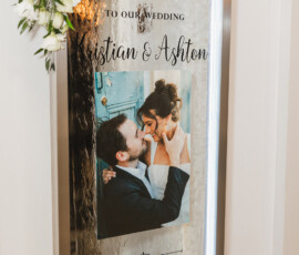 Wedding sign with flowers and couple’s photo reads: Welcome to our wedding, Kristian & Ashton, May 31, 2025.