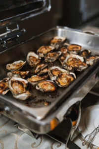 Grilled oysters with savory toppings on a stainless tray, ready to serve at an elegant New Orleans wedding buffet.