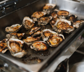 Grilled oysters with savory toppings on a stainless tray, ready to serve at an elegant New Orleans wedding buffet.