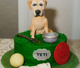 Dog-themed cake with a dog figure topper, green grass-like icing, and playful treats—perfect for fun Louisiana weddings.
