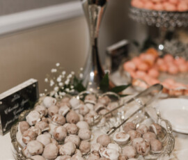 Cake balls in white and milk chocolate on a glass platter at a wedding reception, with tongs, flowers, and pink treats nearby.