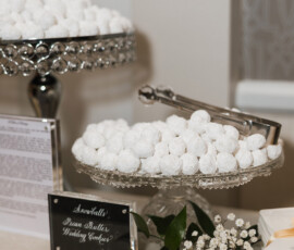 White powdered cookies in glass trays with metal tongs and a floral bouquet. Sign: Snowballs Pecan Butter Wedding Cookies.