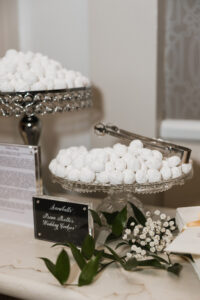 White powdered cookies in glass trays with metal tongs and a floral bouquet. Sign: Snowballs Pecan Butter Wedding Cookies.