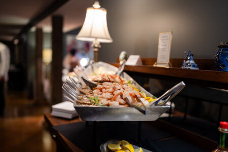 Shrimp and seafood on ice with lemon slices and tongs on a buffet table, warmly lit for a New Orleans wedding reception.
