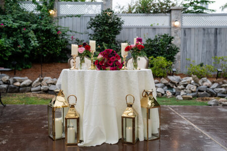 Elegant outdoor wedding table with white cloth, candles, gold lanterns, and floral greenery backdrop in New Orleans.