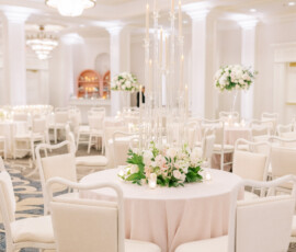Banquet hall with pink table linens, white chairs, floral centerpieces, and chandeliers—ideal for Louisiana weddings.