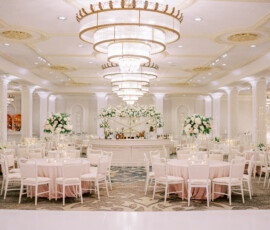 Luxurious New Orleans ballroom with round tables, white chairs, floral centerpieces, and grand chandeliers—ideal wedding venue.
