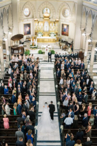 Overhead view of the wedding ceremony as the bride walks down the aisle toward the altar inside a historic church.