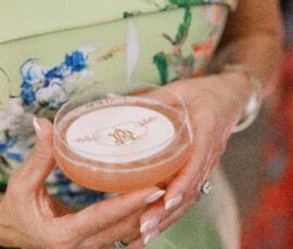 Close-up of a signature cocktail topped with a custom monogram foam garnish, held in a coupe glass.