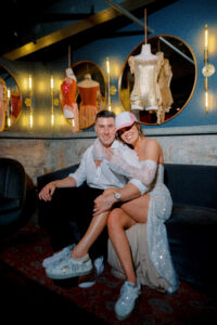 Bride and groom relaxing together on a velvet lounge sofa during the reception, smiling beneath warm ambient lighting and display décor.