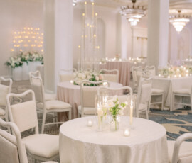 Chic event space with round tables, white linens, candles, floral centerpieces, and chandeliers for a romantic wedding feel.