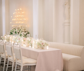 Elegant dining table with pink tablecloth, white chairs, cream sofa, candles, flowers—ideal for a New Orleans wedding.