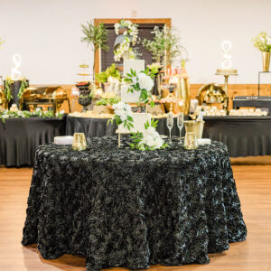 Elegant Louisiana wedding table with black tablecloth, floral cake, gold candles, champagne, and festive buffet in background.