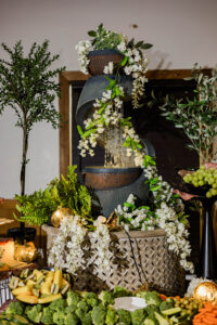 Tiered water fountain with cascading white flowers, greenery, fruit, and vegetables creates a festive Gulf South wedding display.