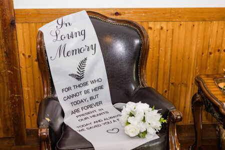 Black leather chair with In Loving Memory sash and white flowers, set by a wood wall—classic New Orleans wedding tribute.
