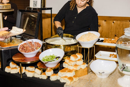Woman serving buffet with mashed potatoes, toppings, fried chicken, dinner rolls, and water at Gulf South wedding reception.
