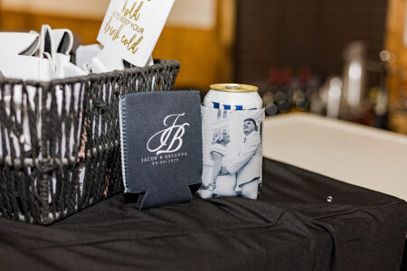 Personalized white and black drink holders on a black tablecloth at a Louisiana wedding, with custom can and date details.