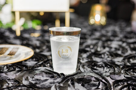A gold-rimmed glass with “J & B 9.6.2025” sits on a black tablecloth at an elegant New Orleans wedding event.