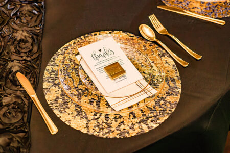 Elegant gold and black dinner setting with clear plate, thank you card, and chocolate at a New Orleans wedding.
