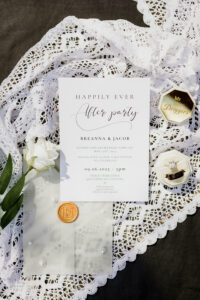 New Orleans wedding invitation, lace, white rose, ring box, and gold-sealed envelope in sunlight—elegant Gulf South details.