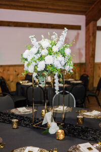 Elegant white rose and greenery centerpiece on black and gold table, rustic wood venue—ideal Louisiana wedding reception.