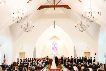 Bride and groom at altar in a bright Louisiana church, wedding party on each side, chandeliers above, audience seated.
