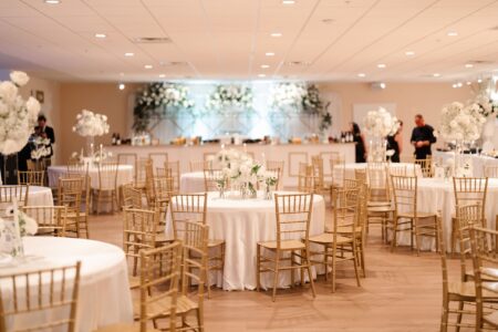 Banquet hall with white-clothed round tables, gold chairs, floral centerpieces, and decorated bar—ideal for Louisiana weddings.