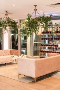 Elegant lounge with beige velvet sofas, floral accents, greenery chandeliers, and bottle shelves—ideal for Louisiana weddings.