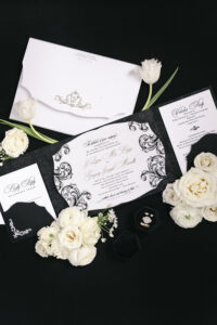 Elegant black and white wedding invitation suite with florals, rings, and formal calligraphy styling.