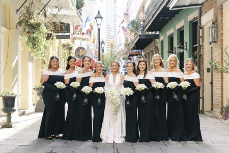 Bride poses with her bridesmaids in matching black off-the-shoulder gowns on a classic New Orleans street.