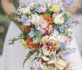 Bride holding a cascading bouquet of pastel blooms with orchids and garden-style florals.