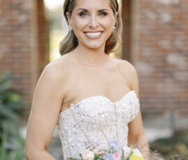 Bride holding a colorful spring bouquet, standing beneath a brick archway in natural light.