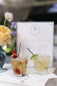 Signature cocktails displayed with garnishes beside a custom drink menu during the wedding reception.