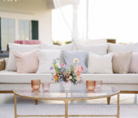 Reception lounge seating with white sofas, pastel accent pillows, and a glass coffee table topped with a floral arrangement.