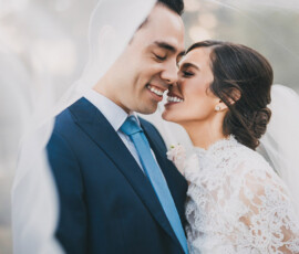 Bride and groom smile under a sheer white veil in formal attire, capturing the romance of a classic New Orleans wedding.