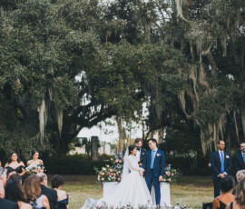 Bride and groom at outdoor wedding with flowers, guests, and trees—ideal inspiration for a picturesque celebration.