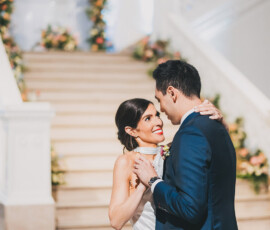 Bride and groom joyfully dance by a flower-adorned staircase in soft, romantic light at a timeless Louisiana wedding.
