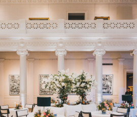 Chic Louisiana wedding venue with white-clothed round tables, black chairs, floral centerpieces, art-lined walls, and a balcony.