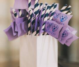 Striped straws with purple flags in a white container, cute dog face and “WE DO TOO!”—fun Louisiana wedding inspo.