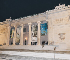 Neoclassical museum at night with tall columns, sculpted friezes, banners, and people on steps—popular New Orleans wedding venue.