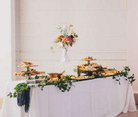 Elegant buffet table with food trays, greenery, and tall flowers on a white cloth—perfect Gulf South wedding inspiration.