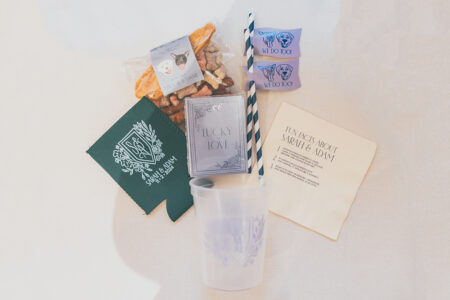 Gulf South wedding welcome kit with snacks, blue straws, green drink sleeve, purple mints, clear cup, and fun fact napkin.